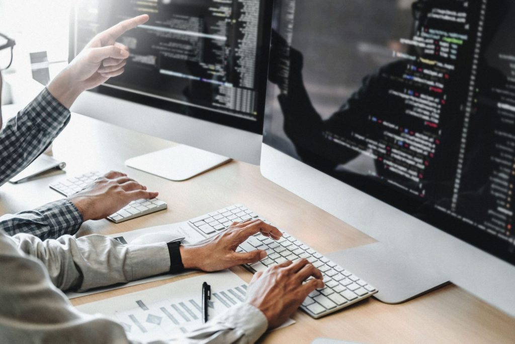 Two people collaborating on code and data analysis at a computer, illustrating real-time inventory and revenue management for rail operations"