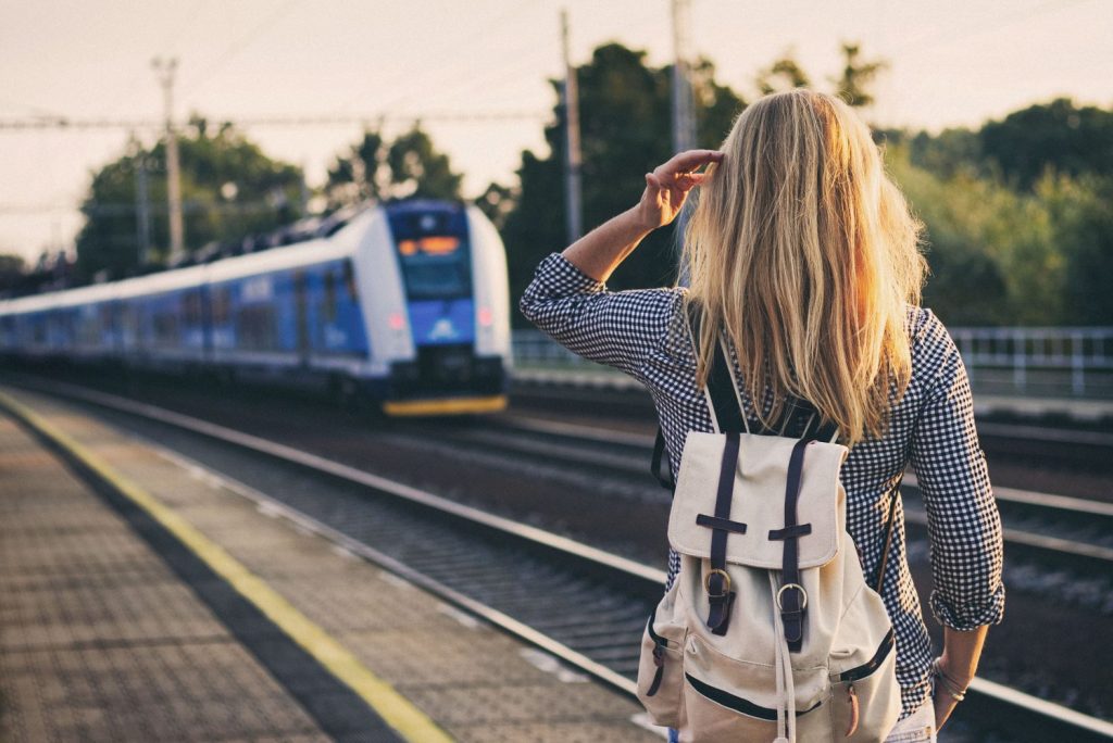 A woman with a backpack waiting at a train station as a train approaches, symbolizing travel demand influenced by scheduled events.